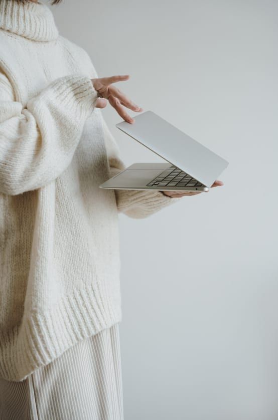 A woman in a cream knit jumper holding an open laptop