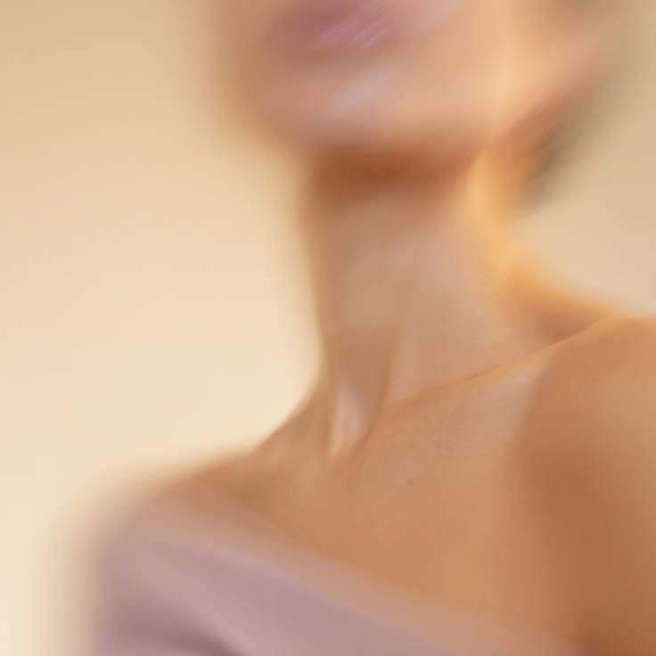 A soft, blurred close-up of a woman’s neck and shoulder in warm light